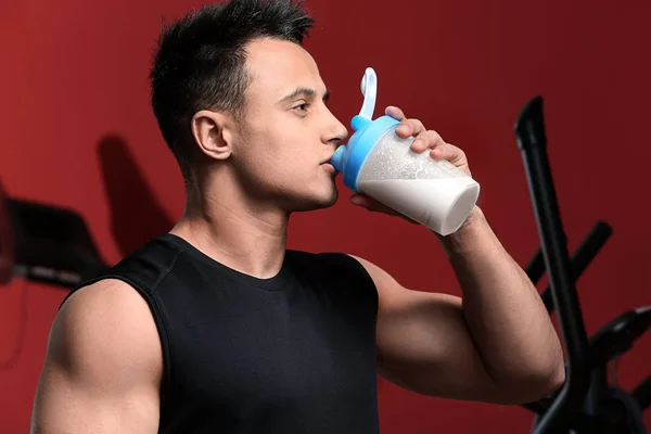 Sporty man drinking protein shake on color background — Stock Photo, Image