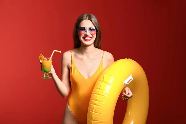 Mooie jonge vrouw met opblaasbare ring en cocktail op kleur achtergrond — Stockfoto