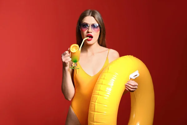 Surprised young woman with inflatable ring and cocktail on color background — Stock Photo, Image