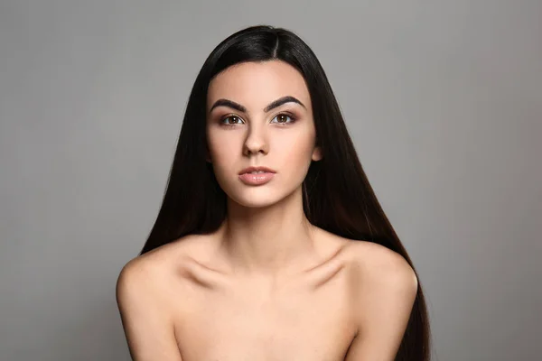 Portrait of beautiful young woman with healthy long hair on grey background — Stock Photo, Image