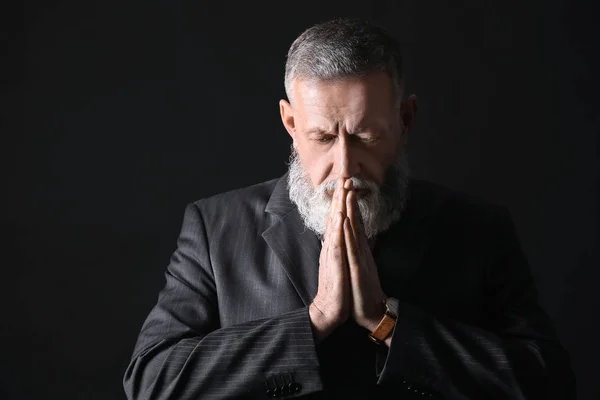 Красивый зрелый бизнесмен молится на тёмном фоне — стоковое фото