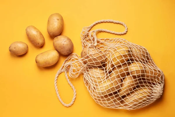 String bag with raw potatoes on color background