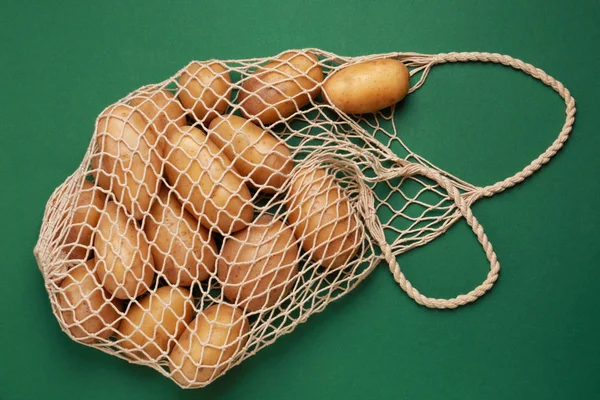 String bag with raw potatoes on color background