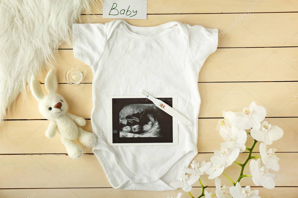 Ropa de bebé, prueba de embarazo, juguete y flores sobre fondo de
