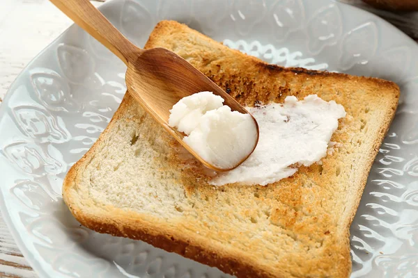 Tasty toasted bread with coconut oil and scoop on plate, closeup — Stock Photo, Image