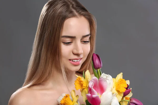 Beautiful young woman with laminated eyelashes and flowers on grey background