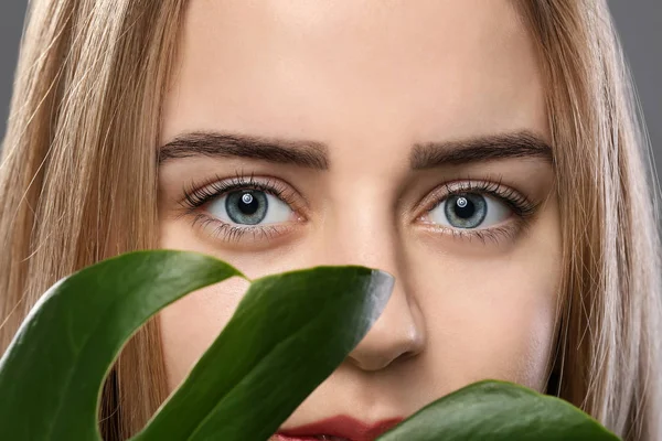 Beautiful young woman with laminated eyelashes and tropical leaf, closeup