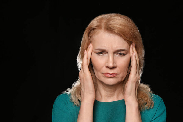 Mature woman suffering from headache on dark background