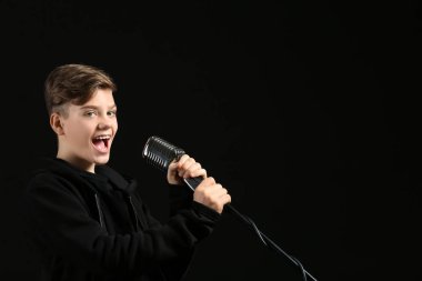 Karanlık arka plan aleyhine şarkı söyleyen mikrofonlu genç çocuk