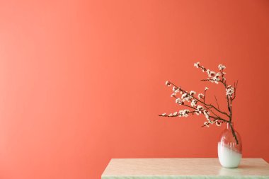 Masanın üzerinde renk arkaplanına karşı çiçek açan güzel dalları olan vazo