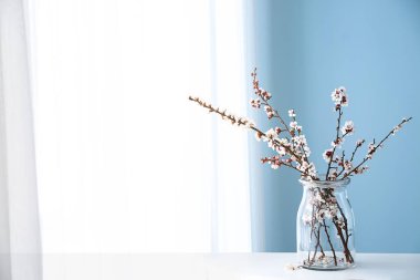 Pencerenin yanındaki masanın üzerinde çiçek açan güzel dalları olan vazo.