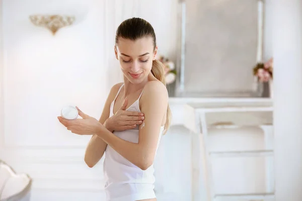 Hermosa joven aplicación de crema corporal en casa — Foto de Stock