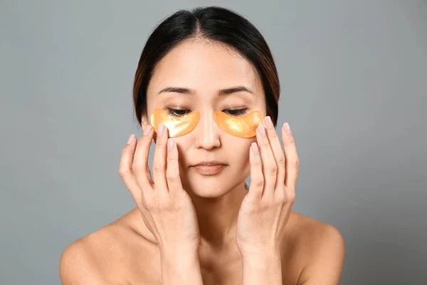 Asian woman with under-eye patches on grey background — Stock Photo, Image