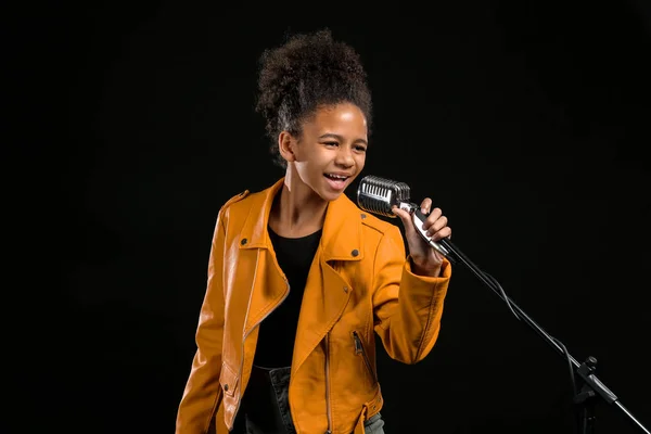 Αφροαμερικάνικη κοπέλα με μικρόφωνο που τραγουδά ενάντια στο σκοτεινό φόντο — Φωτογραφία Αρχείου