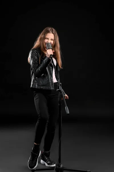 Teenage girl with microphone singing against dark background — Stock Photo, Image