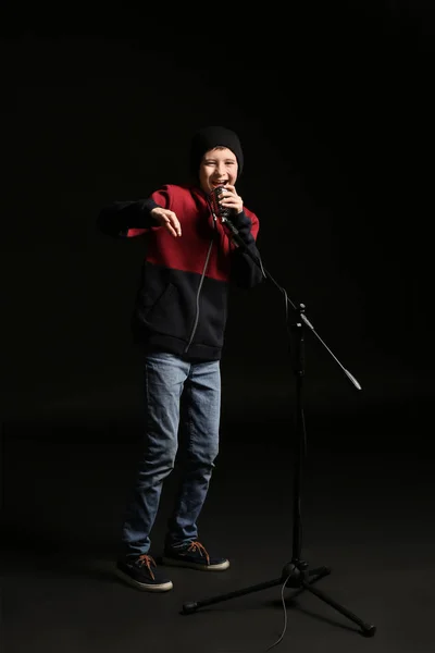 Teenage boy with microphone singing against dark background — Stock Photo, Image