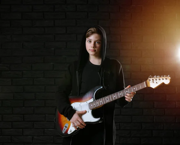 Teenage boy playing guitar against dark wall — Stock Photo, Image