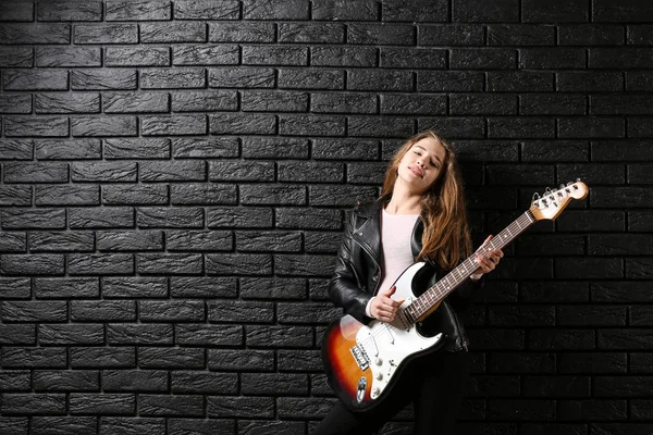 Ragazza adolescente che suona la chitarra contro il muro scuro — Foto Stock