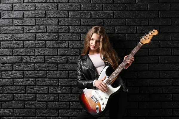 Chica adolescente tocando la guitarra contra la pared oscura — Foto de Stock