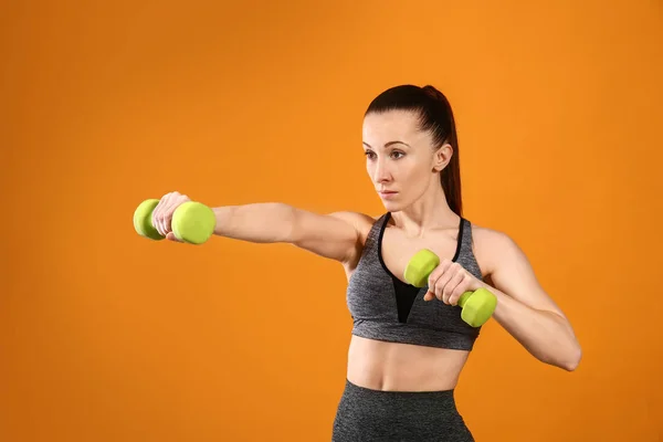 Спортивная женщина тренируется с гантелями на цветном фоне — стоковое фото