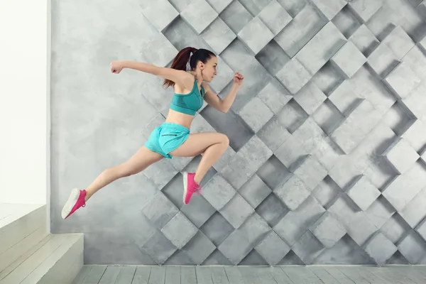 Sporty running woman against grey wall — Stock Photo, Image