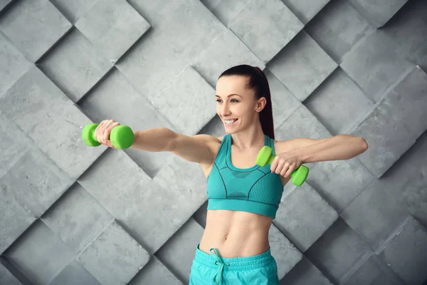 Sporty woman training with dumbbells against grey wall — Stock Photo, Image