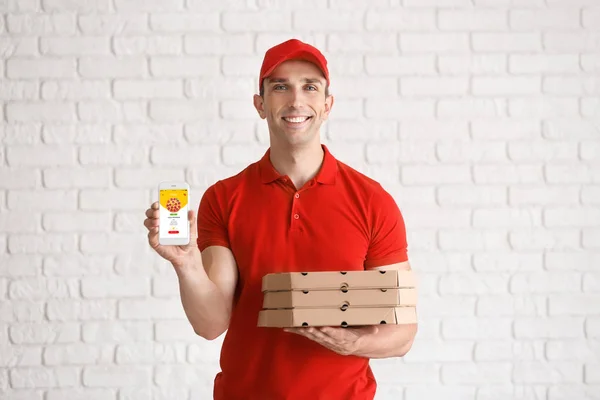 Jovem segurando caixas de pizza e telefone celular com página aberta do site de entrega de alimentos na tela perto da parede de tijolo branco — Fotografia de Stock
