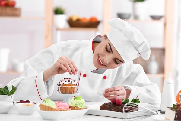 Young female confectioner decorating cupcake in kitchen — Stock Photo, Image