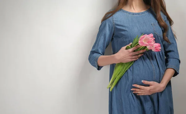 Piękna kobieta w ciąży z kwiatami na jasnym tle — Zdjęcie stockowe