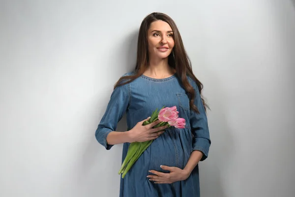 Femeie gravidă frumoasă cu flori pe fundal deschis — Fotografie, imagine de stoc