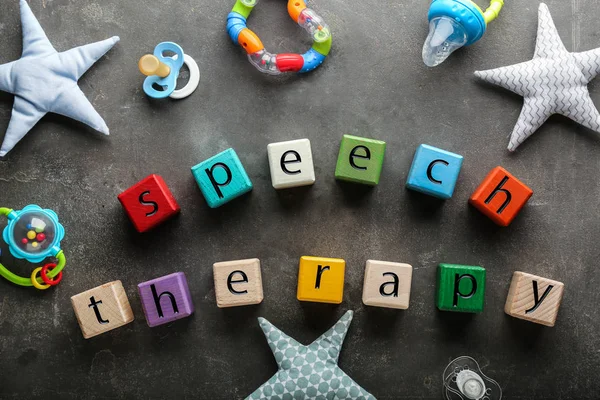 Cubes with text SPEECH THERAPY, pacifiers and toys on grey background