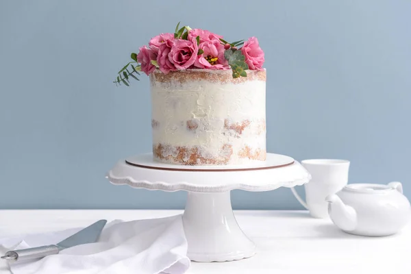 Sweet cake with floral decor on table against color background — Stock Photo, Image