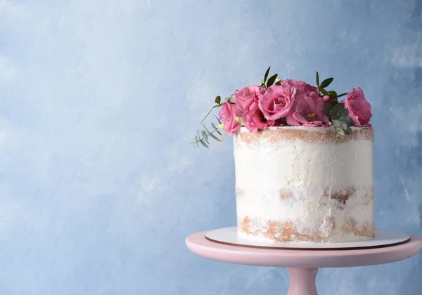 Sweet cake with floral decor on stand against color background — Stock Photo, Image