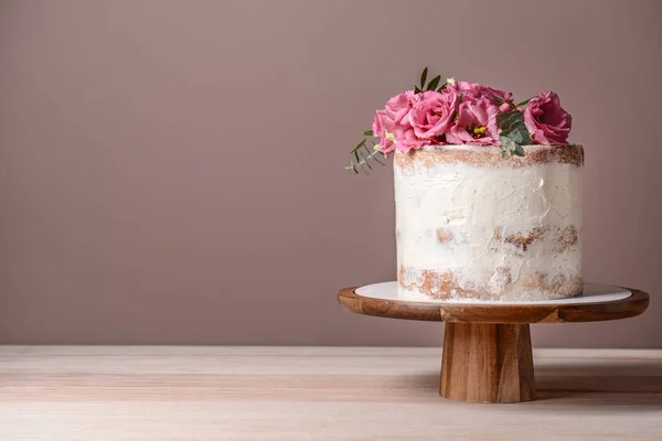 Sweet cake with floral decor on table against color background — Stock Photo, Image