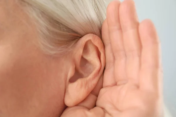 Mujer madura con problemas de audición sobre fondo claro, primer plano — Foto de Stock
