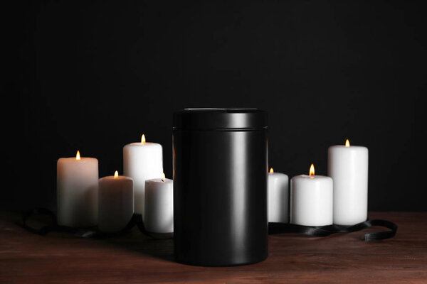 Mortuary urn with burning candles on table against dark background