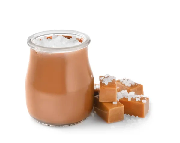 Jar van smakelijke gezouten karamel met snoepjes op witte achtergrond — Stockfoto