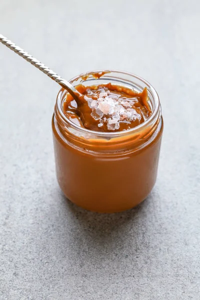 Jar of tasty salted caramel on grey background — Stock Photo, Image