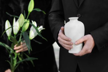 Couple with mortuary urn and flowers at funeral clipart