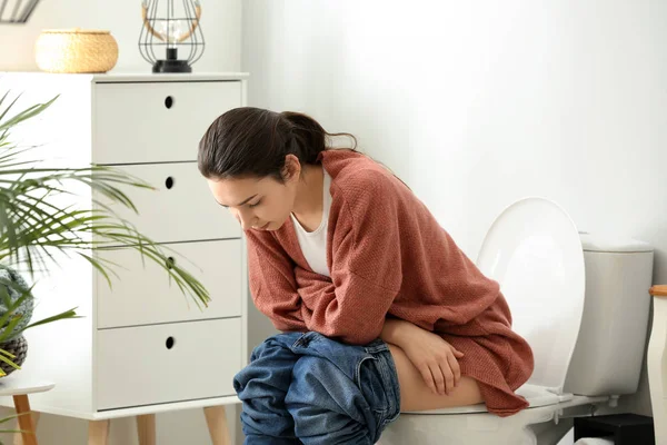 Young woman sitting on toilet bowl in restroom — Stock Photo, Image