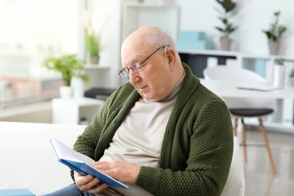 Senior man met gehoorapparaat lezen boek thuis — Stockfoto