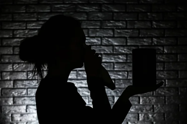 Silhouette of crying woman with mortuary urn on dark brick background — Stock Photo, Image