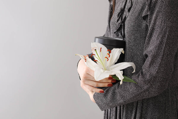 Woman with mortuary urn and lily flower on light background