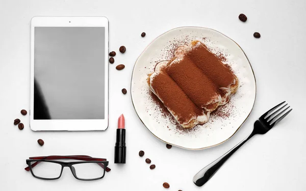 Leckeres Tiramisu mit Tablet-PC, Brille und Lippenstift auf weißem Hintergrund — Stockfoto