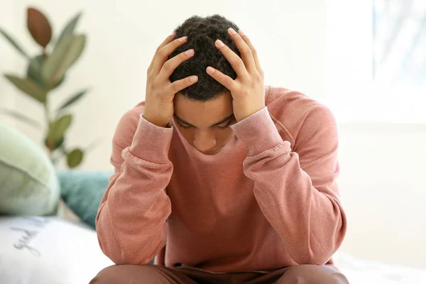 Sad African-American teenage boy sitting on bed at home — Stock Photo, Image