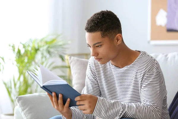 African-American teenage boy reading book at home — Stock Photo, Image