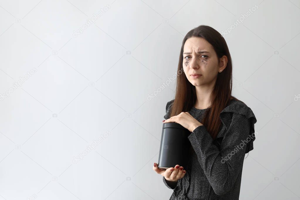 Crying with mortuary urn on light background