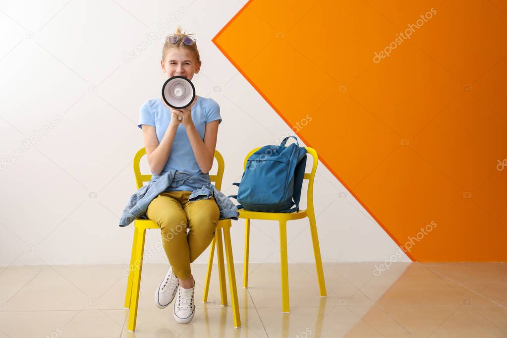 Portrait of cute teenage girl with megaphone sitting on chair near color wall