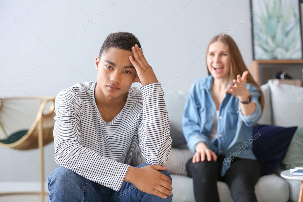 Sad African-American teenage boy having argument with his mother at home