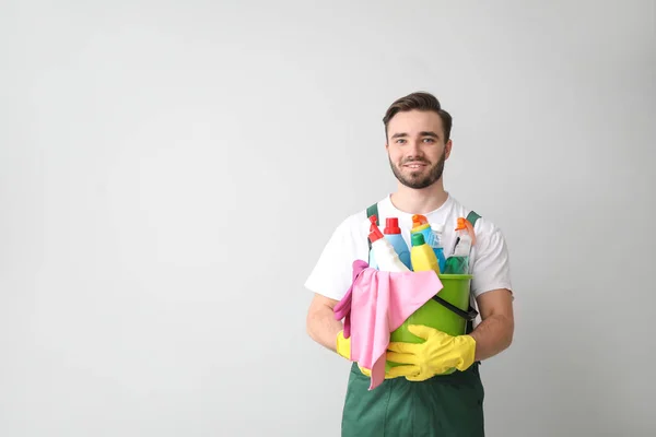 Portrait of male janitor with cleaning supplies on light background — Stock Photo, Image